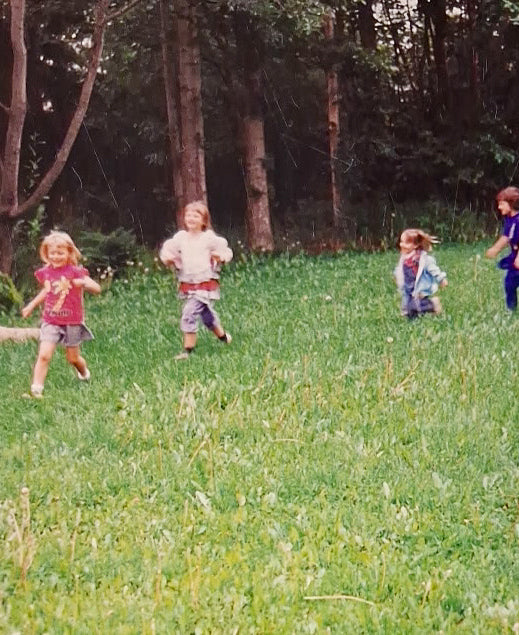 Children running in a grassy field with trees in the background