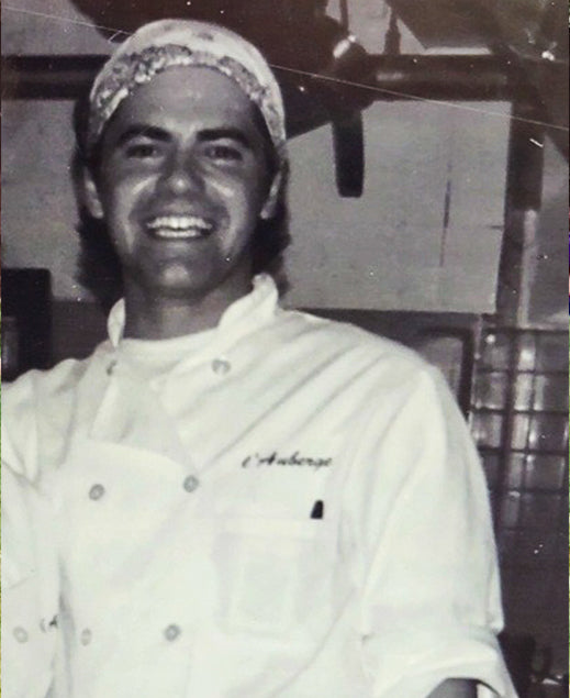 Black and white photo of a person wearing a chef's coat with 'L'Auberge' branding.