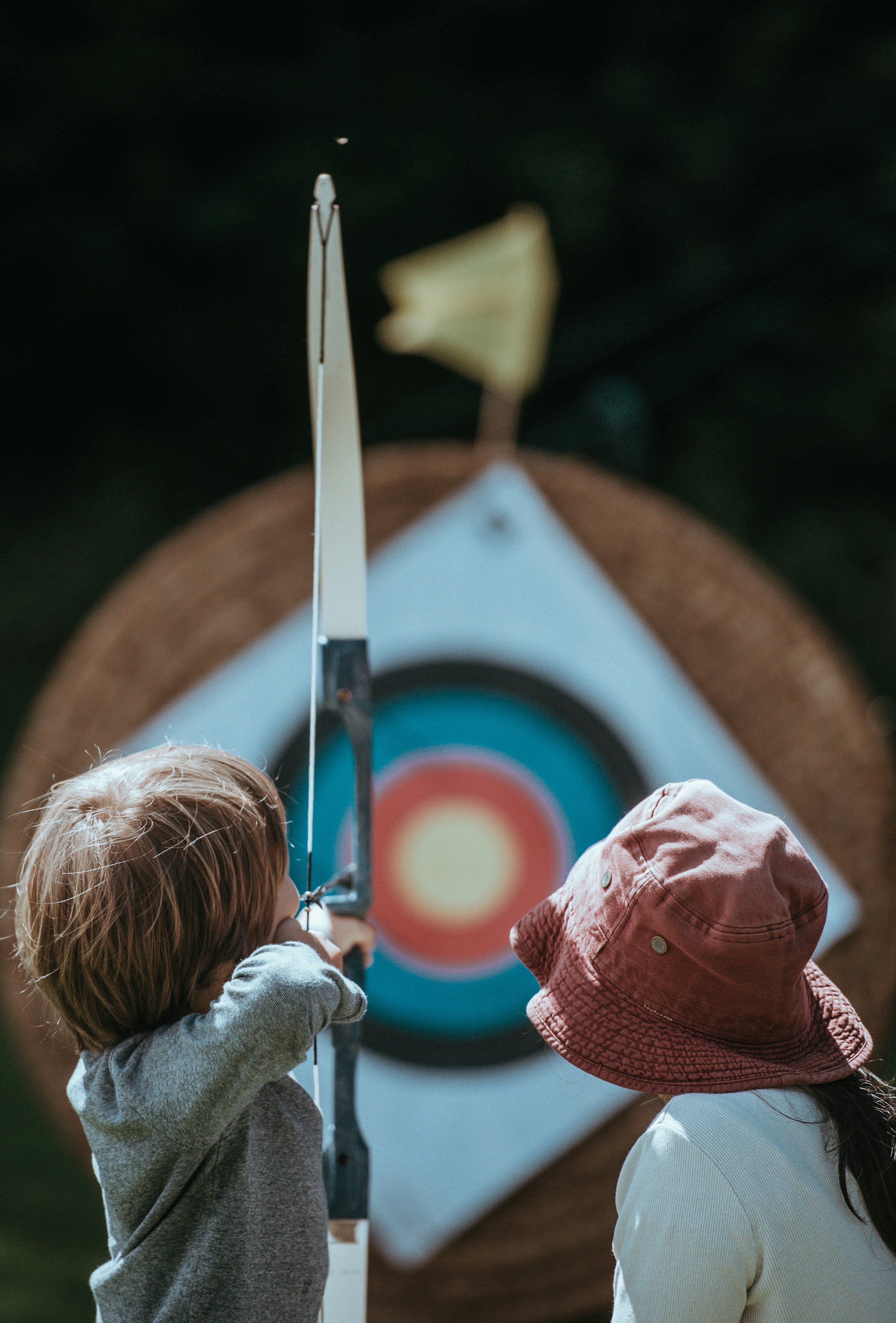 Two children with archery equipment aiming at a target